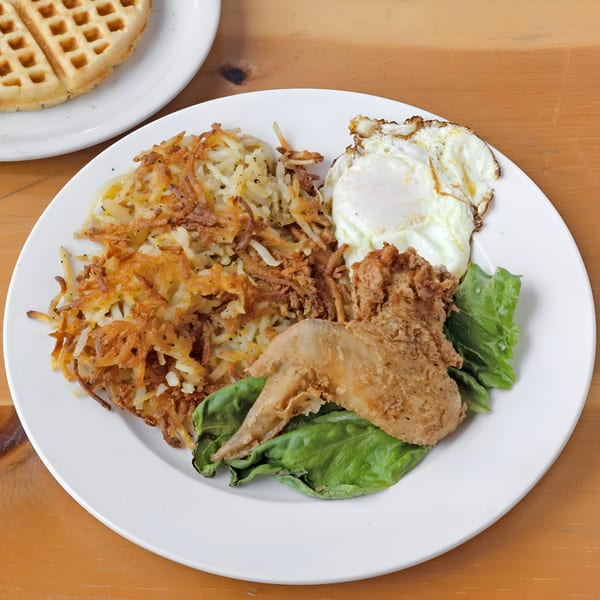 Fried chicken wing, hash browns, and fried egg on a white plate with a waffle.