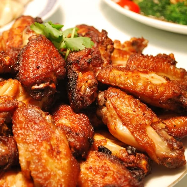 Close-up of crispy, golden-brown chicken wings garnished with fresh cilantro on a white plate.