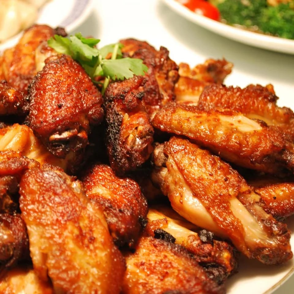 Close-up of crispy, golden-brown chicken wings garnished with fresh cilantro on a white plate.