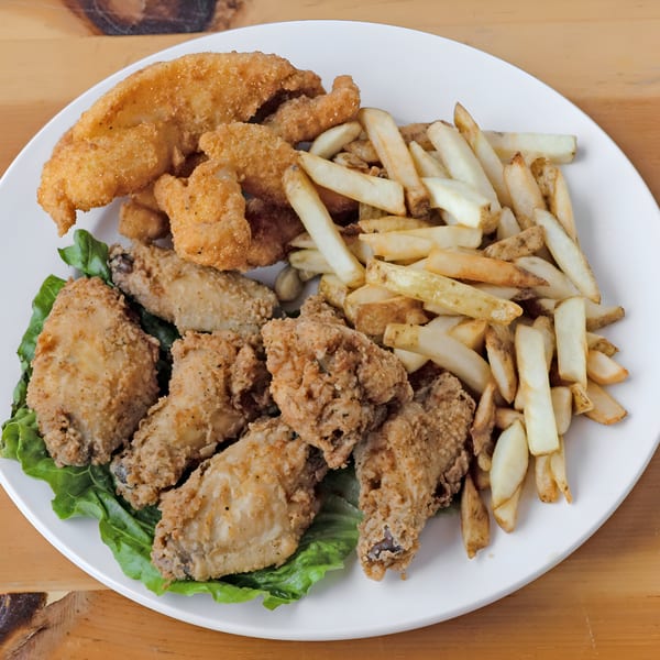 A white plate holds fried chicken wings, fish, and french fries on a bed of lettuce.