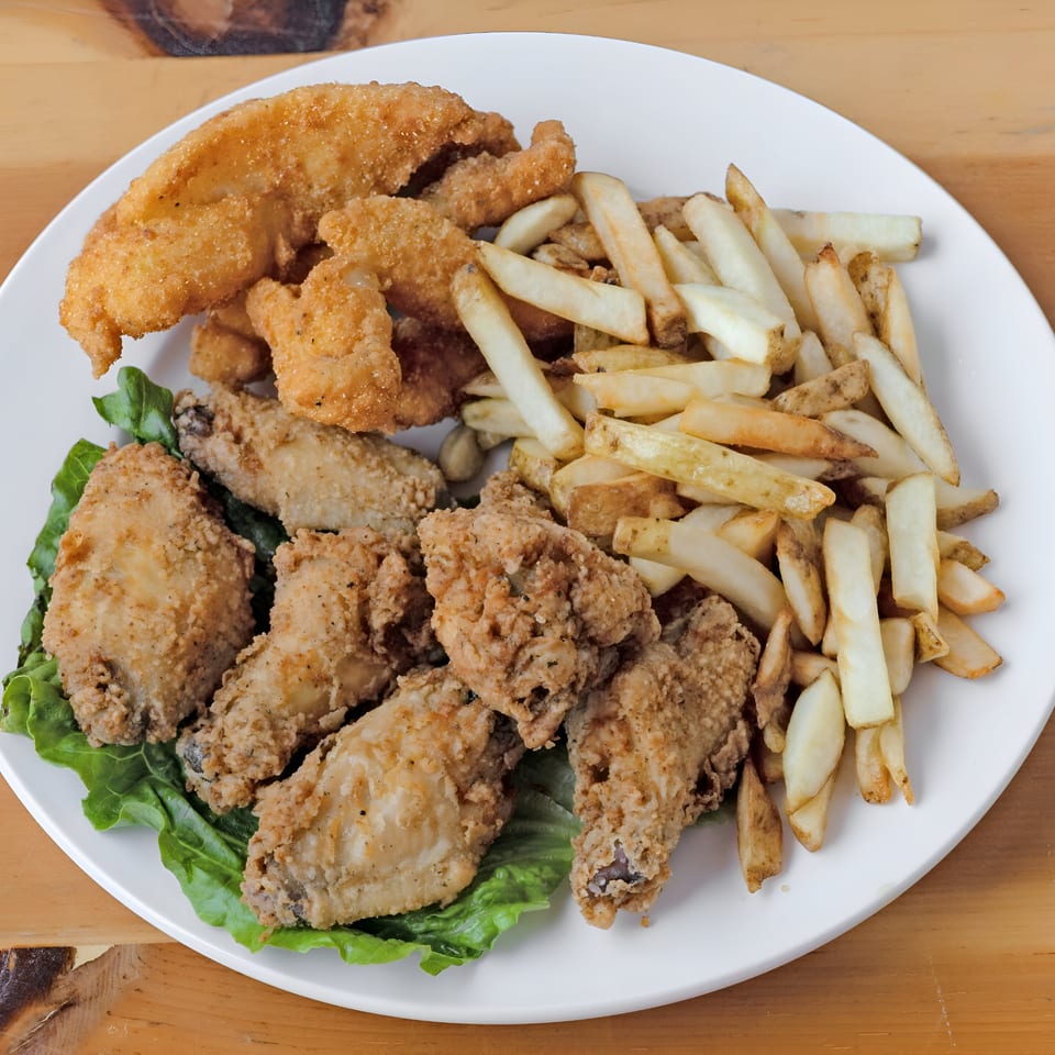 A white plate holds fried chicken wings, fish, and french fries on a bed of lettuce.