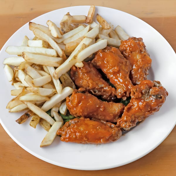 A white plate holds Game Day Chicken Wings and Fish's buffalo wings and a pile of french fries.