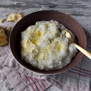 Creamy grits topped with a pat of butter, served alongside a freshly baked biscuit.