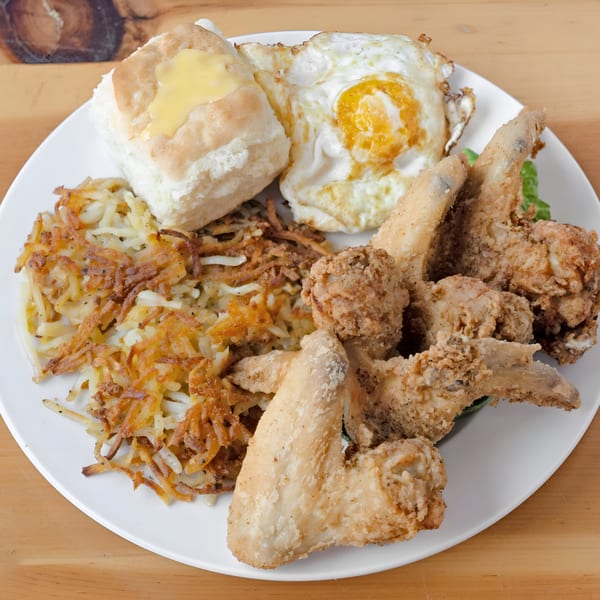 A breakfast plate with fried chicken wings, hash browns, a biscuit with butter, and a fried egg.