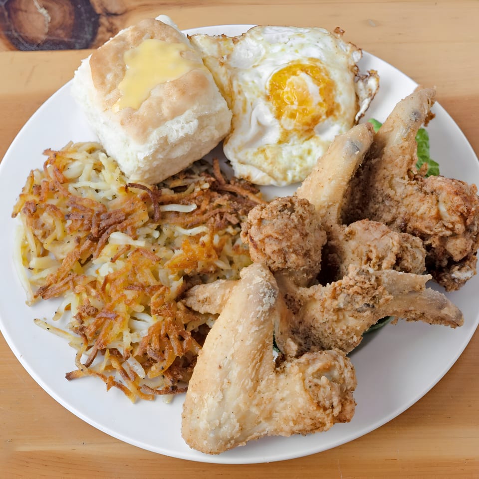 A breakfast plate with fried chicken wings, hash browns, a biscuit with butter, and a fried egg.