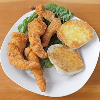 Crispy breaded catfish fillet accompanied by golden-brown toast on a bed of fresh lettuce.