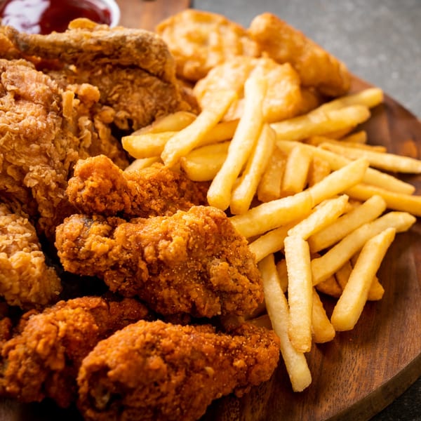 A wooden board piled high with crispy fried chicken, fish, and golden french fries.