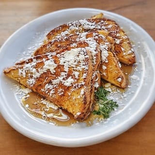 Golden-brown pancakes dusted with powdered sugar and drizzled with syrup.