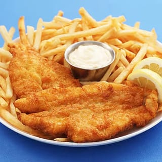 Tilapia fillet, breaded and fried, accompanied by a side of golden fries, tartar sauce, and a lemon wedge