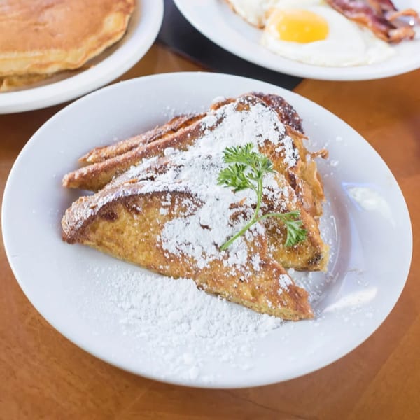 Golden French toast triangles dusted with powdered sugar and a sprig of parsley on a white plate.
