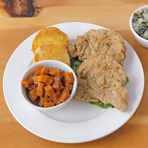Fried fish fillets with two pieces of toast and a side of candied yams on a white plate.