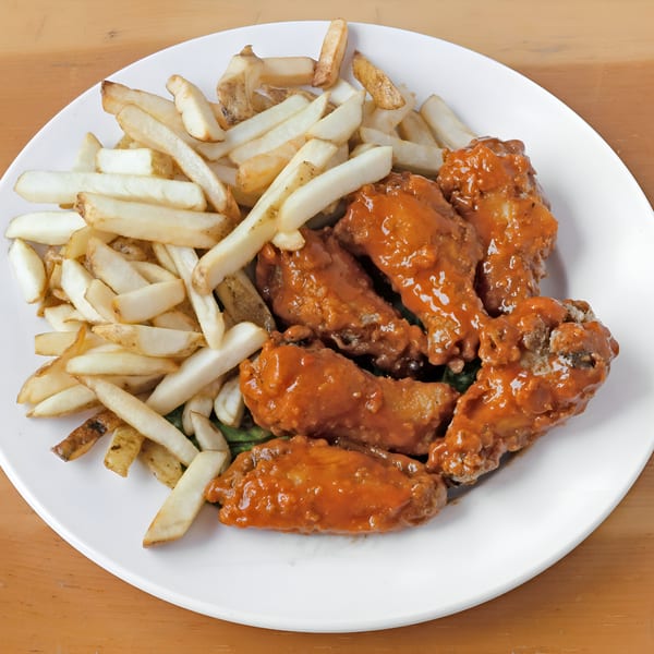 A white plate holds Game Day Chicken Wings and Fish's buffalo wings and a pile of french fries.